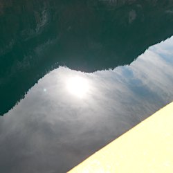 Felswand, Sonne und Wolken spiegeln sich im See